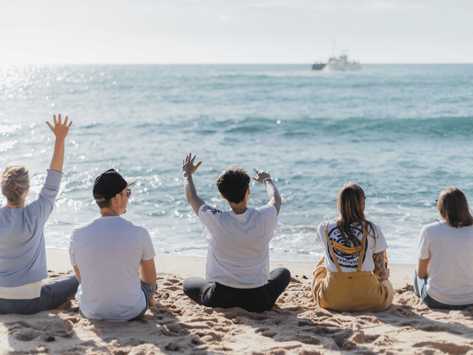 Image showing five employees of the Factorial team sitting on the beach and facing the ocean.