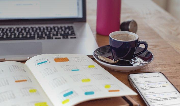 Notizbuch mit Agenda/Kalender, Kaffee und Telefon auf einem Tisch, der die Rolle von dpa-Agenda bei der Planung von Medienberichten und PR-Strategien repräsentiert.