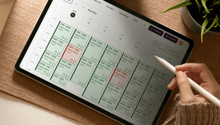 Sicht von oben auf einen Schreibtisch, auf dem die Hand einer Person einen Stift hält und auf einem Tablet arbeitet.