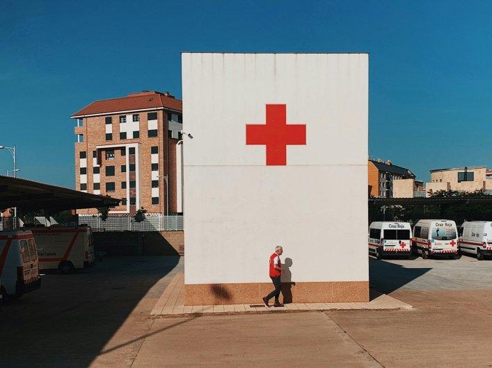 Krankenhauseinfahrt mit einer weißen Mauer und einem roten Kreuz darauf.