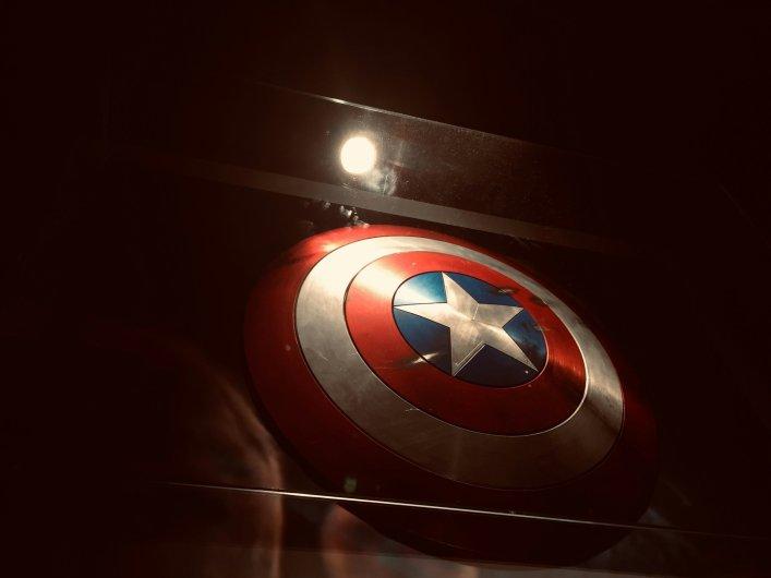 Ausstellung von Captain Americas ikonischem rot-weiß-blauen Schild unter einem Spotlicht in dunkler Umgebung.