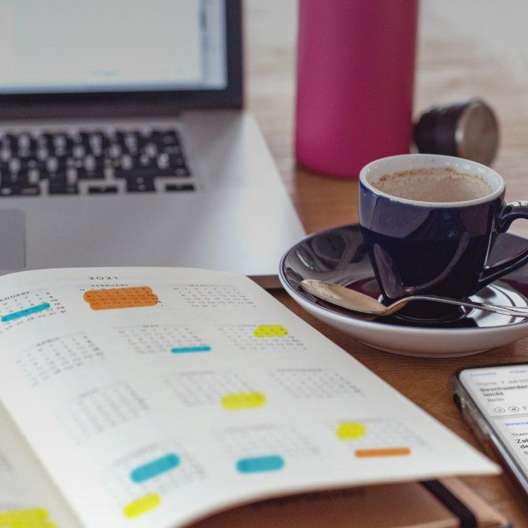 Notizbuch mit Agenda/Kalender, Kaffee und Telefon auf einem Tisch, der die Rolle von dpa-Agenda bei der Planung von Medienberichten und PR-Strategien repräsentiert.