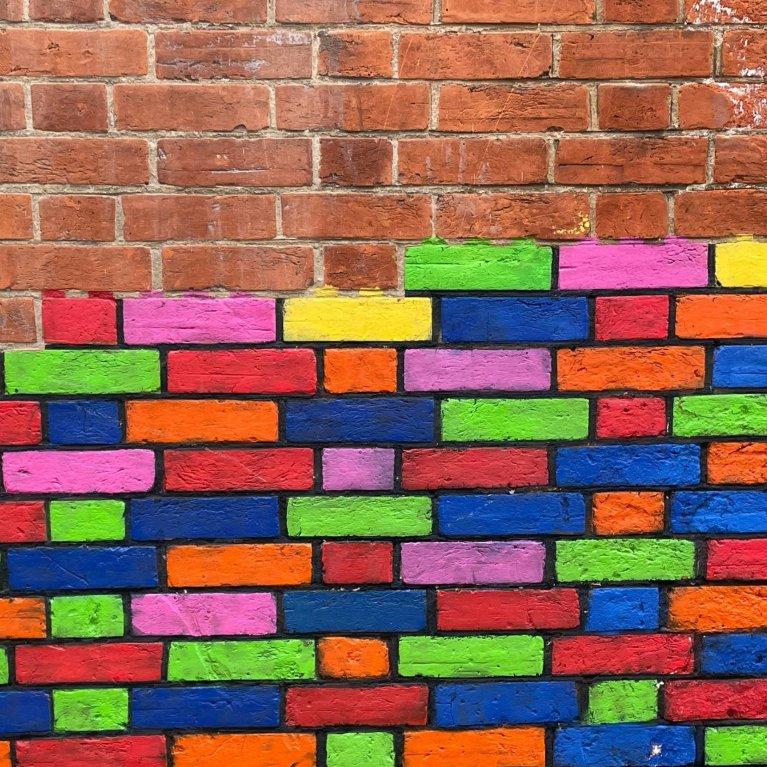 Mann stellt bunte Bausteine zu einer strukturierten Wand – Symbol für strukturiertes Wissens-management mit einem Learning Content Management System.