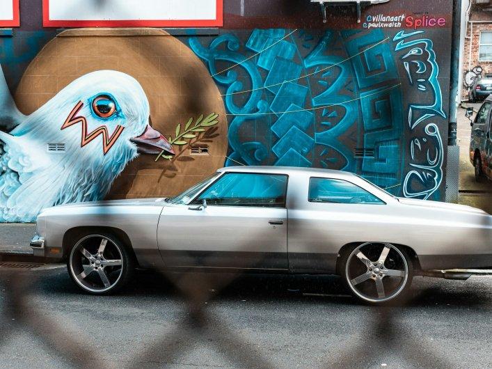 Aufnahme durch Zaun auf ein Auto vor einer Wand mit kunstvollem Graffiti
