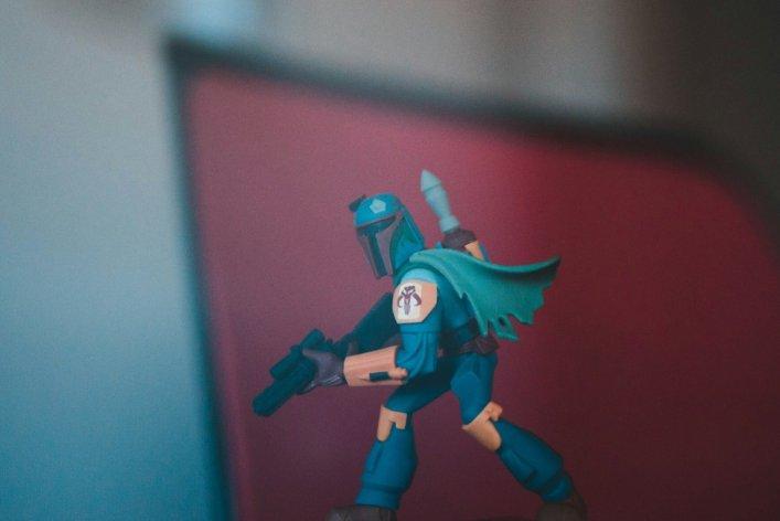 Actionfigur eines Charakters im Mandalorianer-Stil vor einem unscharfen roten Hintergrund.